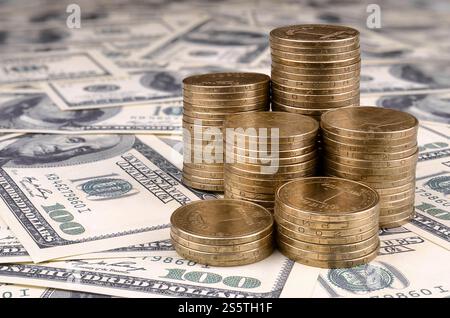 Crescono pile di monete ucraine in pile crescenti. Il denaro ucraino giace su banconote da cento dollari. Il denaro ucraino giace su molte centinaia di dollari Foto Stock