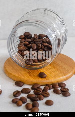 Aggiungere i chicchi di caffè in una tazza di vetro su una base di legno isolata su sfondo bianco Foto Stock