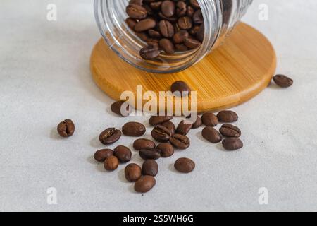 Aggiungere i chicchi di caffè in una tazza di vetro su una base di legno isolata su sfondo bianco Foto Stock