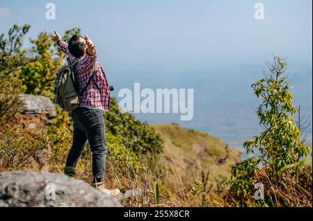 Vista laterale, giovane escursionista asiatico in piedi e alzarsi in mano con felice sulla vetta della montagna rocciosa, splendido paesaggio sullo sfondo, spazio copia Foto Stock