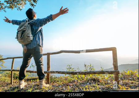 Vista posteriore del giovane escursionista asiatico in piedi al punto di osservazione e alzarsi le mani con felice sulla montagna di picco, copia spazio Foto Stock