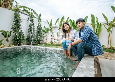 La giovane coppia asiatica si diverte insieme mentre riposa vicino alla piscina, nella nuova casa, il giovane e bello uomo abbraccia la spalla della moglie, concetto di famiglia felice Foto Stock