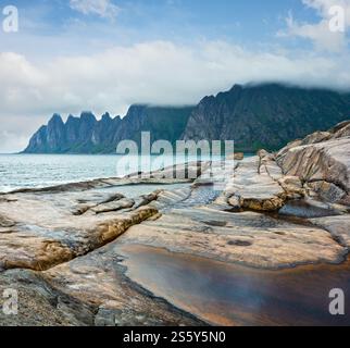 La spiaggia sassosa con bagni di marea a Ersfjord, Senja, Norvegia. Estate giorno polare notte costa. I denti di drago di roccia nel lontano. Foto Stock