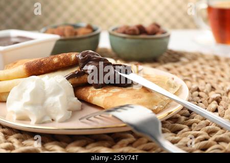 Deliziose crepe con pasta di cioccolato e panna montata sul tavolo, primo piano Foto Stock