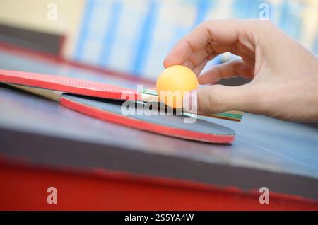 La mano maschile tiene la palla da ping pong su un piccolo tavolo da tennis da vicino in un cortile sportivo all'aperto. Concetto di sport attivi e allenamento fisico. Maniglie maschili Foto Stock
