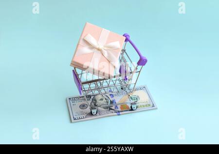 La confezione regalo di un piccolo carrello si trova su una bolletta di un dollaro su sfondo azzurro. La confezione regalo in un piccolo carrello si trova su un dollaro di banconote sulla luce Foto Stock