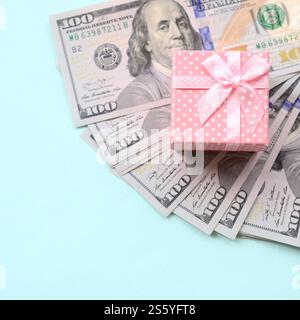 La confezione regalo rosa punteggiata si trova a circa cento banconote da un dollaro su sfondo azzurro. La confezione regalo rosa punteggiata si trova vicino a cento banconote da un dollaro su un blu chiaro Foto Stock