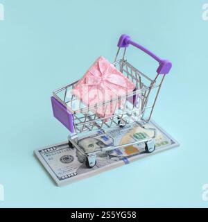 La confezione regalo di un piccolo carrello si trova su una bolletta di un dollaro su sfondo azzurro. La confezione regalo in un piccolo carrello si trova su un dollaro di banconote sulla luce Foto Stock