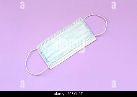 Maschera protettiva medica con fasce auricolari in gomma su sfondo rosa. Maschera chirurgica monouso coprire la bocca e il naso. Assistenza sanitaria e medica Foto Stock