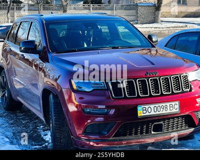 Kiev, Ucraina - 14 gennaio 2025: Un SUV rosso Jeep Grand Cherokee parcheggiato all'aperto in un quartiere sotto la luce del sole durante l'inverno. Foto Stock