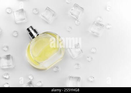 Bottiglia gialla di profumo femminile, fotografia obiettivo della bottiglia di profumo in cubetti di ghiaccio e acqua su un tavolo bianco. Vista dall'alto. Foto del prodotto mockup, Foto Stock