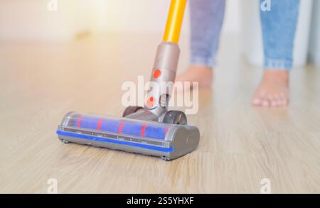 Donna che pulisce il pavimento in legno con un aspirapolvere nel soggiorno. Concetto di pulizia della casa, attenzione selettiva. Foto Stock