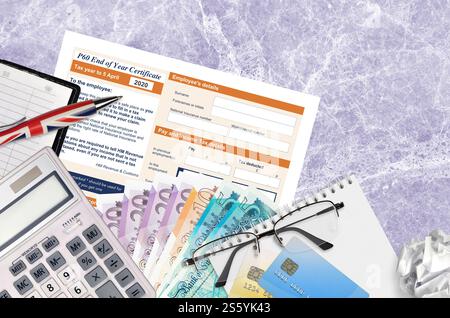 Modulo fiscale inglese P60 certificato di fine anno da HM Revenue and Customs si trova sul tavolo con gli articoli per ufficio. Documentazione HMRC e processo di pagamento delle imposte in Foto Stock