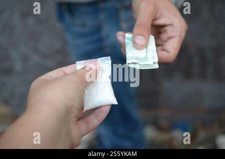 Mano di tossicodipendente con soldi che comprano una dose di cocaina o eroina. primo piano sull'acquisto di dose da parte di tossicodipendenti, traffico di droga, dipendenza da crimine Foto Stock