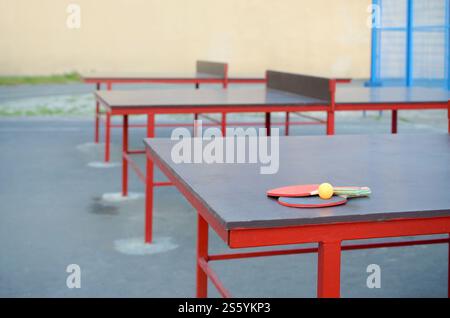 Racchette e palla da vicino sul tavolo da ping pong in un cortile sportivo all'aperto. Concetto di sport attivi e allenamento fisico. Racchette e palla sul tavolo da ping pong Foto Stock