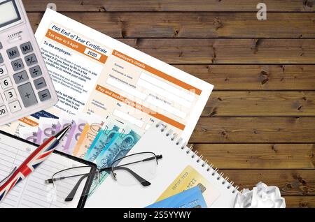 Modulo fiscale inglese P60 certificato di fine anno da HM Revenue and Customs si trova sul tavolo con gli articoli per ufficio. Documentazione HMRC e processo di pagamento delle imposte in Foto Stock