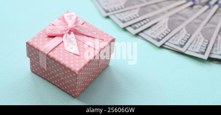 La confezione regalo rosa punteggiata si trova a circa cento banconote da un dollaro su sfondo azzurro. La confezione regalo rosa punteggiata si trova vicino a cento banconote da un dollaro su un blu chiaro Foto Stock