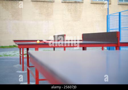 Racchette e palla da vicino sul tavolo da ping pong in un cortile sportivo all'aperto. Concetto di sport attivi e allenamento fisico. Racchette e palla sul tavolo da ping pong Foto Stock