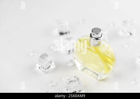 Bottiglia gialla di profumo femminile, fotografia obiettivo della bottiglia di profumo in cubetti di ghiaccio e acqua su un tavolo bianco. Vista dall'alto. Foto del prodotto mockup, Foto Stock