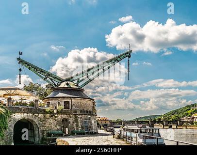 Una pittoresca scena sul lungofiume con una gru storica, una barca ormeggiata e un tranquillo sfondo di un ponte su un bellissimo cielo blu con le macchinine Foto Stock