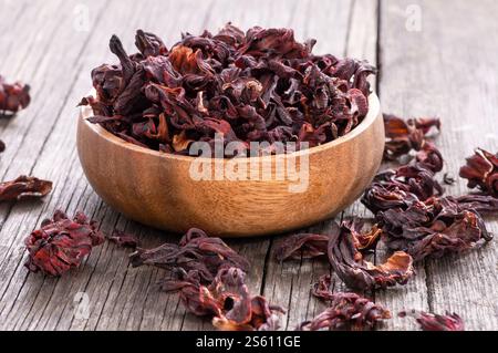 Fiore di ibisco essiccato in cucchiaio di legno o ciotola su tavola di legno, medicina alternativa Foto Stock