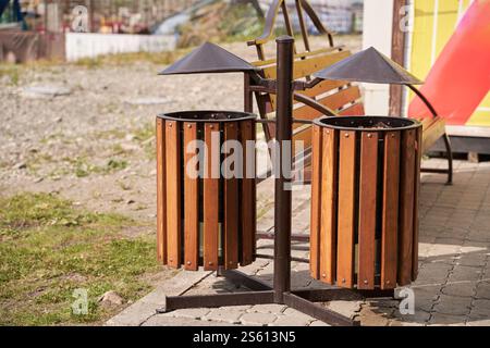 Lattine di spazzatura in legno per esterni su telaio in metallo in ambiente urbano con panca e pavimentazione in pietra. Foto Stock