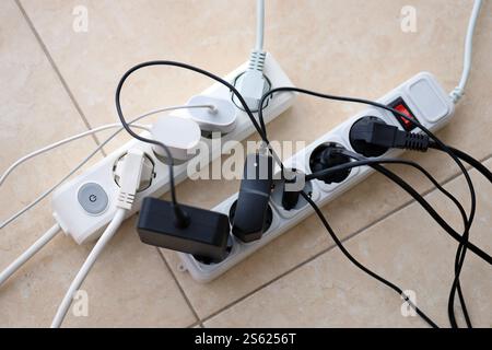 Schede di alimentazione sovraccaricate. Prese multiple con diverse spine elettriche sul pavimento bianco. Concetto di rischio pericolo corrente di sovraccarico elettrico. Foto Stock