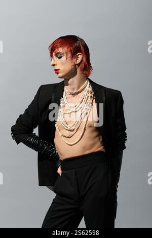 Un giovane uomo con un outfit audace e perle a strati irradia fiducia con un trucco spettacolare. Foto Stock