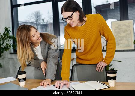 Due giovani professionisti condividono idee e risate mentre lavorano a un progetto in un ufficio moderno. Foto Stock