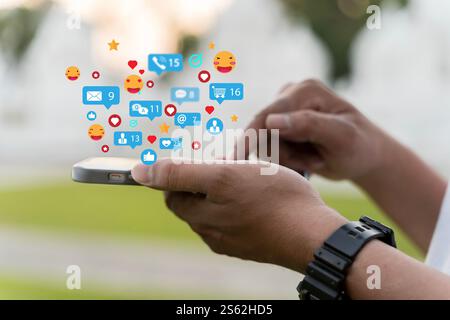 Primo piano di un giovane che controlla la rete di social media sullo smartphone mentre è in movimento in città. Telefono cellulare con messaggio a forma di bolla vocale Heart emoji su sc Foto Stock