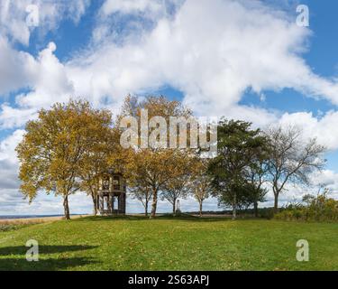 Una foto vibrante che cattura un tranquillo paesaggio autunnale con un piccolo padiglione in pietra, la Indian Tower, con alberi dalla foglia dorata sotto un cielo dinamico. Foto Stock