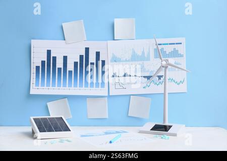 Diagrammi con note adesive vuote e modello di turbina eolica sul tavolo vicino alla parete blu. Concetto di energia verde Foto Stock