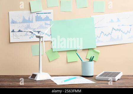 Diagrammi con note adesive vuote e modello di turbina eolica sul tavolo vicino alla parete beige. Concetto di energia verde Foto Stock