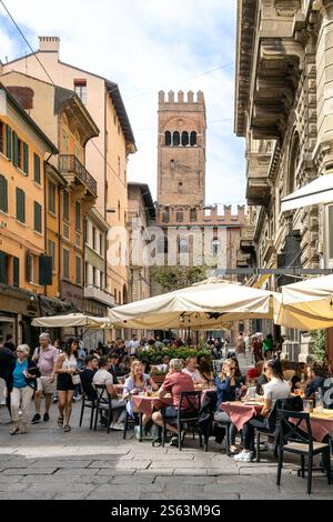 Bologna, Italia - 15 settembre 2024: Strada trafficata con persone che si godono i pasti all'aperto e la Torre dell'Arengo sullo sfondo Foto Stock