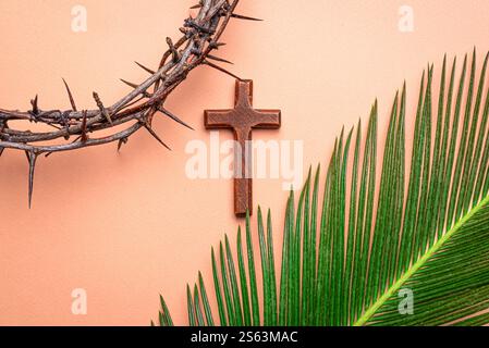 Domenica delle Palme, settimana Santa o modello di Pasqua. Corona di spine, croce di legno e foglia di palma su sfondo rosa arancio. La mattina del cristianesimo festivo Foto Stock