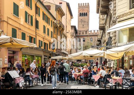 Bologna, Italia - 15 settembre 2024: Strada trafficata con persone che si godono i pasti all'aperto e la Torre dell'Arengo sullo sfondo Foto Stock