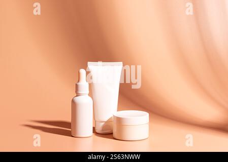 Contenitori per prodotti cosmetici per il viso su sfondo beige arancione, spazio per copie. Bianco vuoto viso crema idratante vaso, maschera nutriente tubo e viso seru Foto Stock
