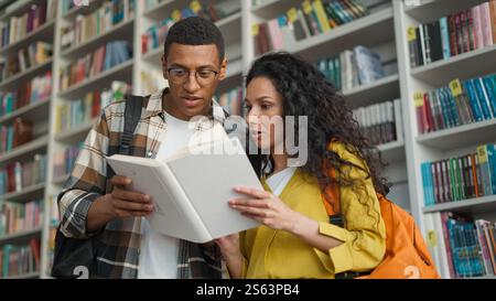Eccitato uomo afroamericano donna latina araba che legge libri studenti della comunità libreria interessante storia apprendimento educazione insieme Foto Stock