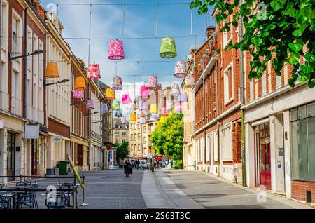 Amiens, Francia, 3 luglio 2023: Donna che cammina lungo la strada pedonale con lanterne cinesi multicolore sopra e edifici in mattoni nella vecchia città storica Foto Stock