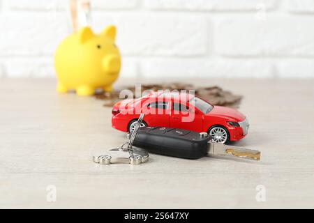 Chiave, modello, salvadanaio e monete su sfondo chiaro, messa a fuoco selettiva Foto Stock