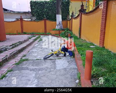 Un bambino latino di 10 anni dalla pelle scura soffre una caduta dalla bicicletta con dolore alle gambe e alle braccia Foto Stock