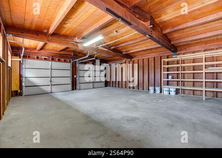 Questo grande garage dispone di un alto soffitto in legno con travi a vista, pavimento in cemento e diversi ripiani. Ideale per parcheggi, officine o. Foto Stock