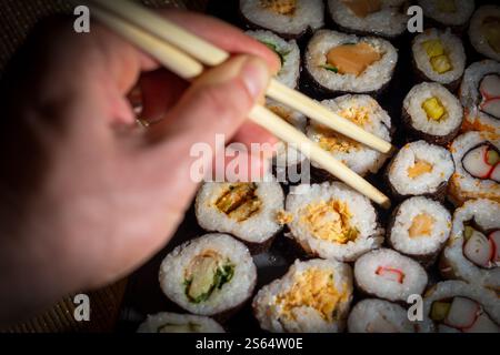 Mano dell'uomo con bacchette di bambù e sushi roll Foto Stock