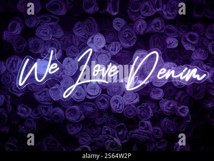 Insegna al neon viola "We Love Denim" davanti allo sfondo dei jeans. Foto Stock