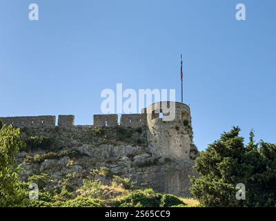Spalato, Croazia - 1° luglio 2024: Fortezza di Klis bastioni occidentali e torre di avvistamento Oprah sotto il paesaggio blu delle nuvole. Alberi verdi e cespugli giù. Bandiera in cima Foto Stock