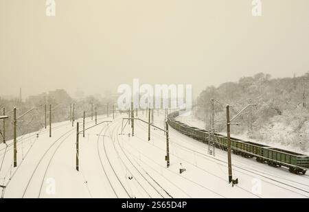Un lungo treno di vagoni merci si muove lungo la ferrovia. Paesaggio ferroviario in inverno dopo le nevicate Foto Stock