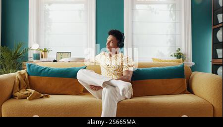 Casa, pensiero e uomo sul divano, cuffie e relax con sorriso, radio e idee nella lounge. Persona, appartamento e ragazzo sul divano, cuffie e ascolto Foto Stock