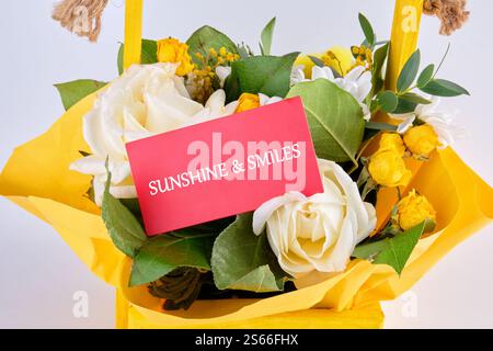 Una vivace composizione di fiori gialli include rose e altri fiori, con una carta che dice Sunshine and Smiles, perfetta per celebrare l'amore. Foto Stock