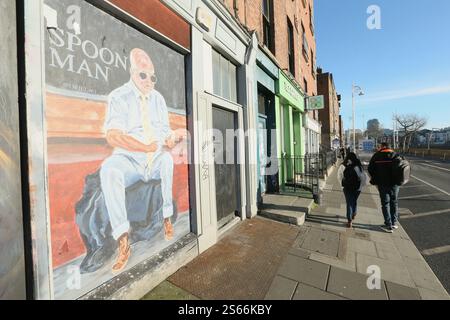 Dublino, Irlanda - 15 gennaio 2025 - le persone passano davanti a un murale di 'spoonman' su una finestra a bordo di un edificio lungo il Liffey nel centro di Dublino mentre la dura luce del sole si abbassa durante il periodo di bel tempo. Foto Stock