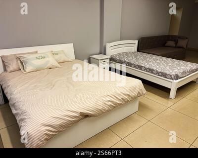 Foto di una camera moderna con due letti e un comodo divano. L'arredamento dello spazio sfoggia una gamma di colori neutri con un design minimalista e accogliente Foto Stock